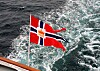 Norsk flagg vaier over et skummende kjølvann bak et fartøy.