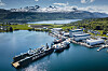 Luftfoto av verft med flere brønnbåter ved kai omgitt av fjord og fjell.