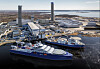 Et stort blått og hvitt fartøy ligger ved kai i et verftsområde med industribygg og vann rundt.